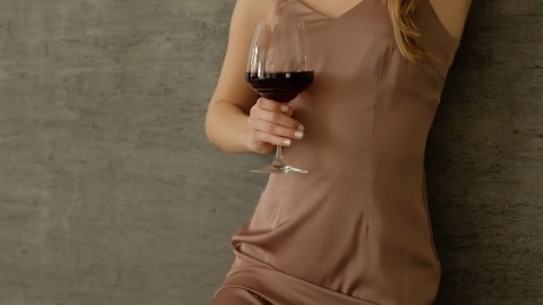 Demostración de ropa nueva en el estudio, chica en ropa de moda de moda. sostiene una gran copa de vino en su mano. de pie junto a la pared — Vídeos de Stock