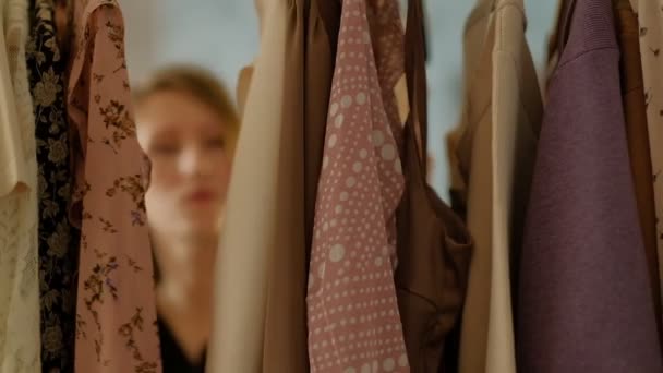 Soft Focus Shot av kläder klänning rack med hängare och outfits. Ung söt flicka försöker välja fashionabla trendiga utseende. Slow motion shot — Stockvideo