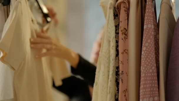 Soft εστίαση βολή της ένδυσης ράφι φόρεμα με κρεμάστρες και ρούχα. Νεαρό όμορφο κορίτσι προσπαθεί να επιλέξει τη μοντέρνα μοντέρνα εμφάνιση. βολή αργής κίνησης — Αρχείο Βίντεο