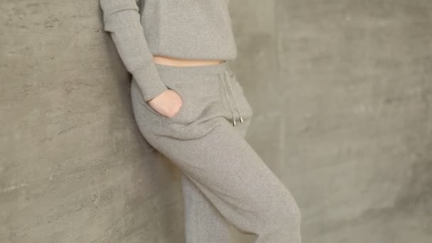 Girl in a gray knit sweatshirt stands against a wall, her hands in her pockets. — Stock Video