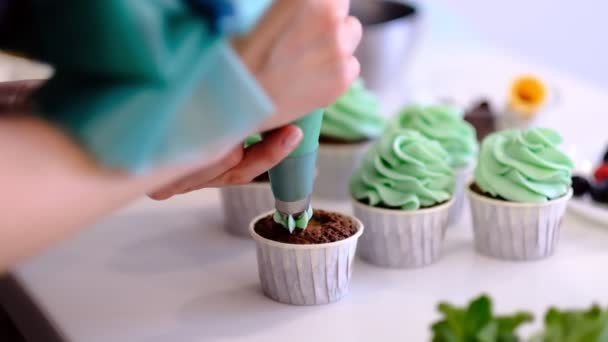 Διακόσμηση Κύπελλο-τούρτα με κρέμα. Χρησιμοποιώντας μαγειρικής σακούλα, ζαχαροπλάστης κάνοντας πολύχρωμα cupcakes για το κόμμα. Στιγμιότυπο από γυναικεία χέρια βάζοντας βούτυρο κρέμα τα νόστιμα κέικ, έννοια σπίτι αρτοποιίας — Αρχείο Βίντεο