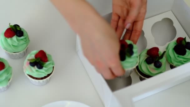 Manos de pastelera femenina empaquetado cupcakes recién hechos con glaseado de crema de mantequilla en caja de regalo y atándolo con cinta, vista de ángulo alto — Vídeos de Stock