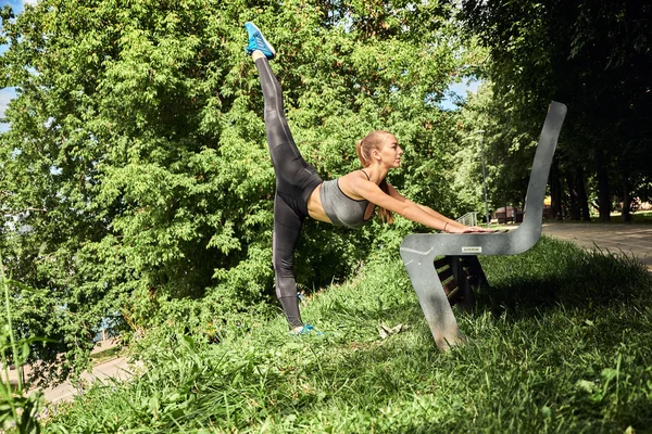 Foto de increíble joven mujer de los deportes en el parque al aire libre hacer ejercicios de estiramiento deportivo. Joven corredor estirándose antes de la carrera de la ciudad — Foto de Stock