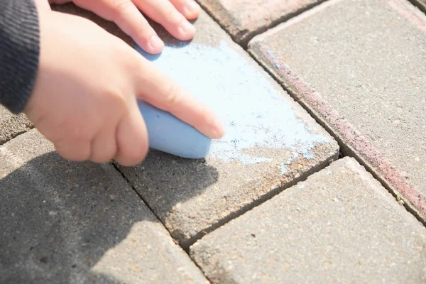 Criança que desenha com giz em asfalto. rapaz a brincar sozinho na rua. segurando um pedaço de giz em seus dedos — Fotografia de Stock