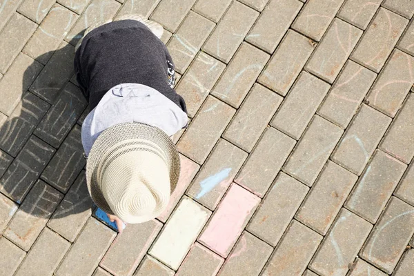 Child drawing with chalk on asphalt. boy playing alone in the street. holding a piece of chalk in his fingers — Stock Photo, Image