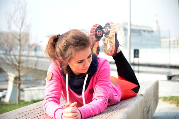 Mujer joven ejercita yoga en la ciudad manos arriba y equilibrándose de pie sobre una pierna en un día soleado . — Foto de Stock