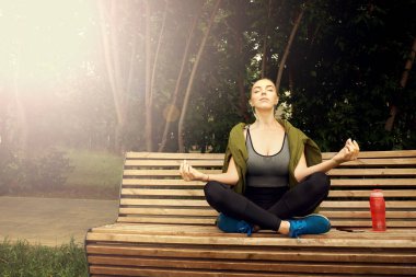 Park'ta yoga yapan beyaz bir kadın. Lotus pozisyonunda oturmak.