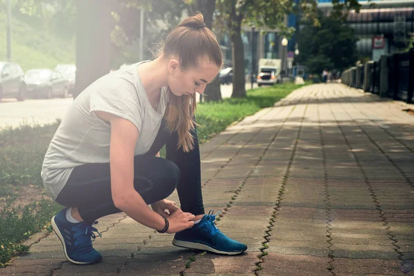 fitness woman tie shoelaces on road. Cheerful runner sitting on floor on city streets with mobile and earphones wearing sport shoes. Active latin woman tying shoe lace before running.