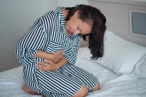 Kaukasische vrouwen dragen witte pyjama liggend in bed slapeloosheid veroorzaakt door migraine ongemak. Geaccumuleerde stress en menstruatie ontspanning dat is niet genoeg om het lichaam te verzwakken moet arts raadplegen. — Stockfoto