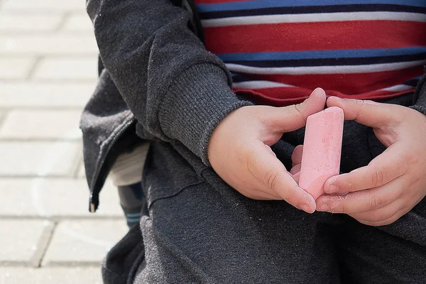 Barn ritning med krita på asfalt. pojken spelar ensam på gatan. håller en bit krita i fingrarna — Stockfoto