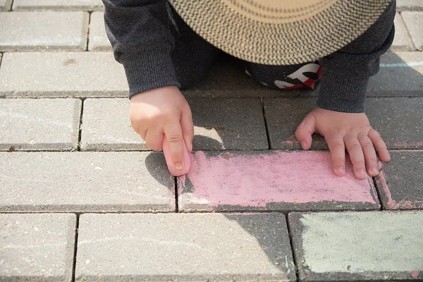 asfalt üzerinde tebeşir ile çocuk çizim. sokakta tek başına oynayan bir çocuk. parmaklarında bir tebeşir parçası tutarak