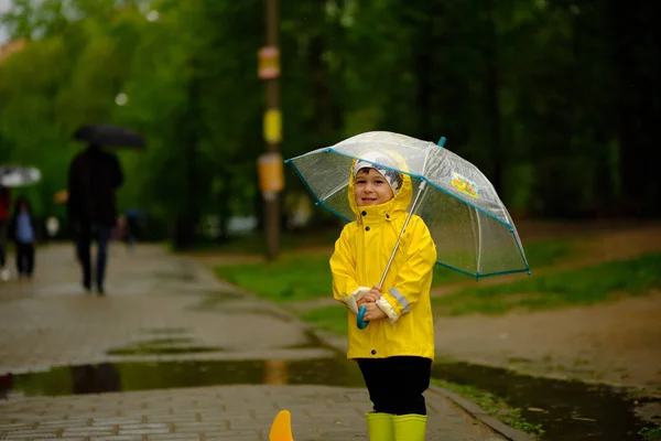 Niedliches Baby, das an einem regnerischen Tag unter einem Regenschirm steht. Ein Junge im gelben Regenmantel spaziert durch den Park. — Stockfoto