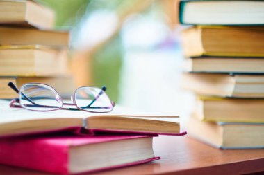 masada vintage kitap yığını, gözlük ve açık bir kitap. arka plan parkı ormanda, sokağa pencereden bir görünüm.