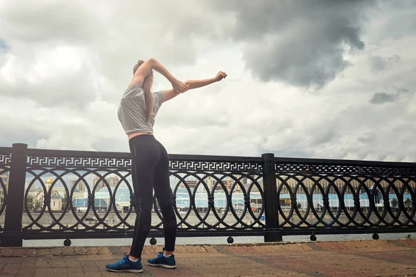 Retrato de mujer joven en forma y deportiva haciendo estiramiento en la ciudad. — Foto de Stock