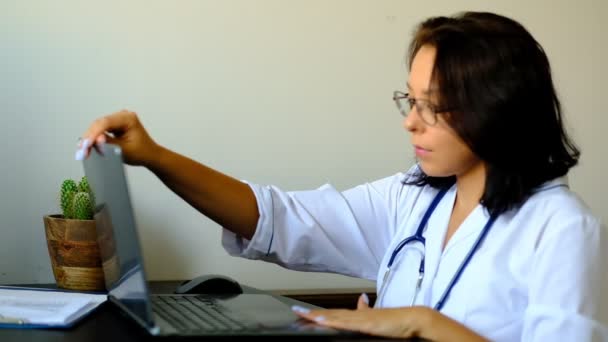 Close-up van onbekende vrouwelijke arts zittend aan de tafel in het ziekenhuis en typen op laptop computer. Jonge vrouw arts verpleegkundige in ziekenhuis kliniek kantoor. — Stockvideo