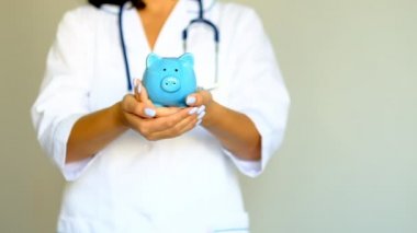 Yavaş çekim yakın çekim. Kadın doktor kumbaranın içine bozuk para koyup, yakından kapatıyor. Sağlık sigortası kavramı