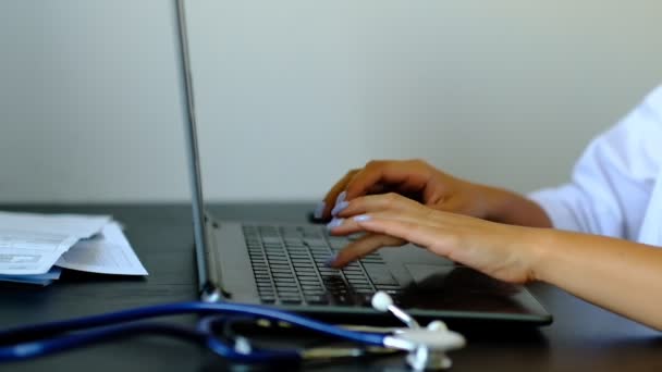 Zwolnionym. Bliska nieznanych kobiet lekarz siedzi przy stole w szpitalu i wpisując na komputerze przenośnym — Wideo stockowe
