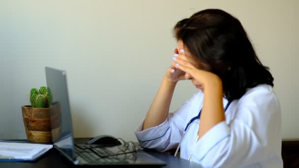 Close-up van onbekende vrouwelijke arts zittend aan de tafel in het ziekenhuis en typen op laptop computer. Jonge vrouw arts verpleegkundige in ziekenhuis kliniek kantoor. — Stockvideo