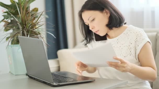 Cámara lenta. Multitarea femenina en el lugar de trabajo. Empresaria que trabaja en la oficina hablando por teléfono celular, revisando un informe financiero y usando computadora portátil . — Vídeos de Stock