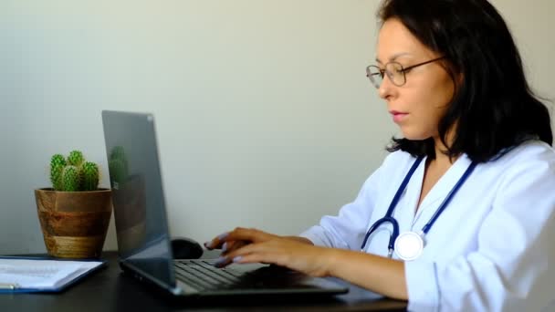 Movimento lento. Close up de médica desconhecida sentada à mesa no hospital e digitando no computador portátil — Vídeo de Stock