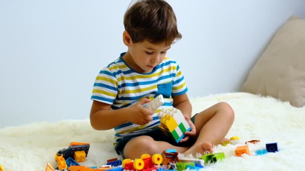 Cámara lenta asiático chico jugando con colorido construcción plástico bloques en blanco cama en casa  . — Vídeos de Stock