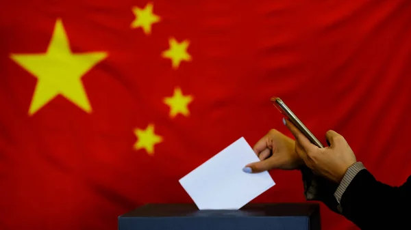 Hand holding ballot paper for election vote concept. elections, The hand of woman putting her vote in the ballot box. China Flag on background.