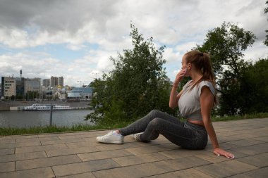 Genç kadın koşucu güneşli sabah egzersiz oturumu sonra dinlenme. Kadın fitness modeli şehirde gölet boyunca sokakta oturan. Kadın koşucu koşu egzersiz bir mola