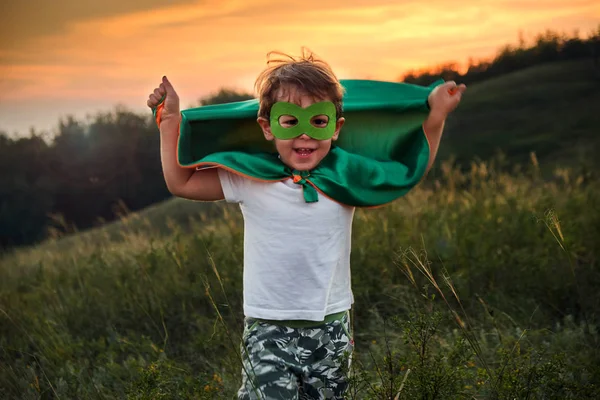 Liten pojke spelar en superhjälte. Kid i en superheros kostym. Happy Child springer för att träffa fotografen. — Stockfoto