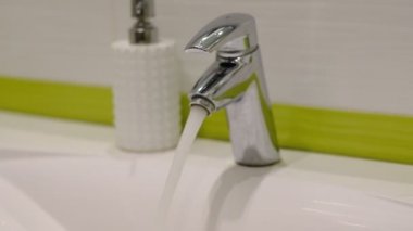 yavaş çekim. Evde banyoda ev işleri yapan kadın, sprey deterjanile lavabo ve musluk temizliği yapıyor. Kırpılmış görünüm