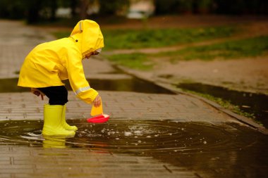 küçük çocuk yağmurlu bir sonbahar gününde bir su birikintisi içinde plastik bir tekne ile oynar.