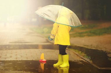 mutlu çocuk bir yaz yağmurlu bir günde bir su birikintisi oynuyor. Sarı yağmurluklu bir çocuk parkta yürüyor..