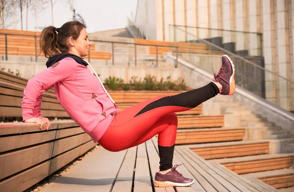 Mujer joven ejercita yoga en la ciudad manos arriba y equilibrándose de pie sobre una pierna en un día soleado . — Foto de Stock