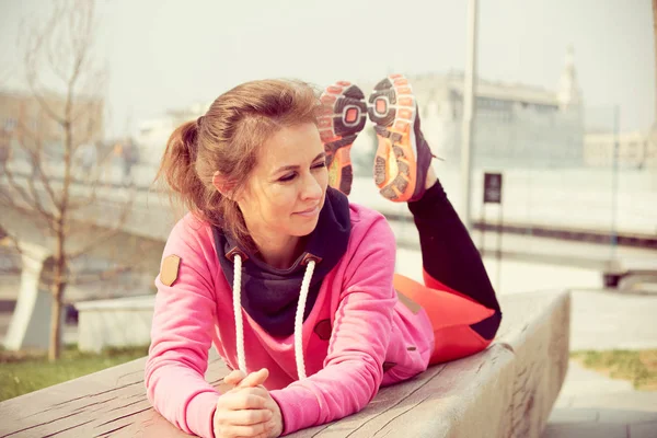 Mujer asiática joven mira hacia otro lado. chica en un chándal rosa se encuentra en su estómago después del entrenamiento deportivo . — Foto de Stock