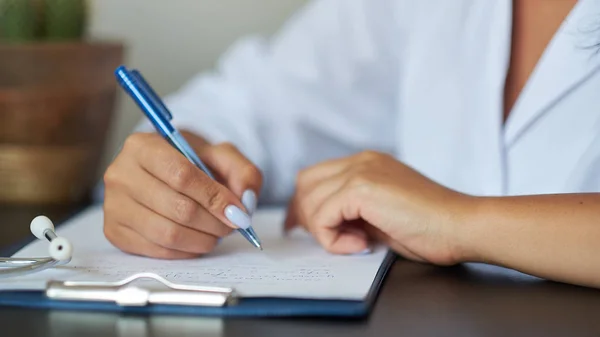 Joven terapeuta llenando la lista médica sentada en el escritorio. Concepto de salud y seguro. Doctora haciendo papeleo en el consultorio . — Foto de Stock