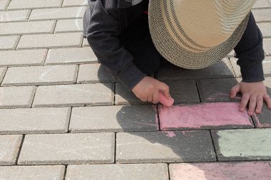 asfalt üzerinde tebeşir ile çocuk çizim. sokakta tek başına oynayan bir çocuk. parmaklarında bir tebeşir parçası tutarak