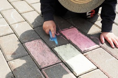 asfalt üzerinde tebeşir ile çocuk çizim. sokakta tek başına oynayan bir çocuk. parmaklarında bir tebeşir parçası tutarak