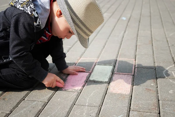 Barn ritning med krita på asfalt. pojken spelar ensam på gatan. håller en bit krita i fingrarna — Stockfoto