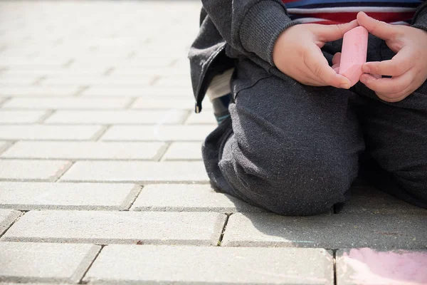 Gyermek rajz kréta az aszfalt. fiú játszik egyedül az utcán. kezében egy darab kréta ujjai — Stock Fotó