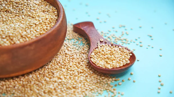 Białe nasiona quinoa na niebieskim tle. Quinoa w misce i łyżkę na stole kuchennym widoku z góry. Zdrowe i dietetyczne produkty Superfood. — Zdjęcie stockowe