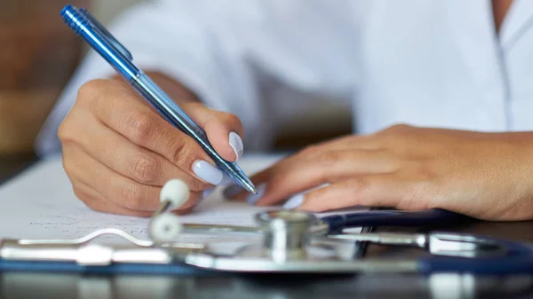 Young therapist filling medical checklist sitting at the desk. Health care and insurance concept. Female doctor doing paperwork in the office.