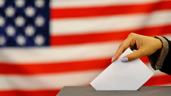 Woman putting a ballot in a ballot box on election day. Close up of hand with white votes paper on usa flag background. — Stock Photo, Image