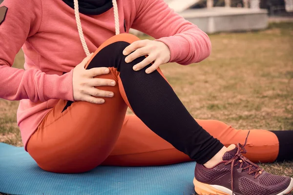 Female athlete suffering form running knee or kneecap injury during outdoor workout on dirt road. — Stock Photo, Image