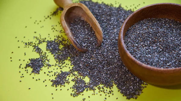 Nutritious chia seeds on a yellow background. chia seeds in bowl and a spoon on kitchen table top view. Healthy and diet superfood product.