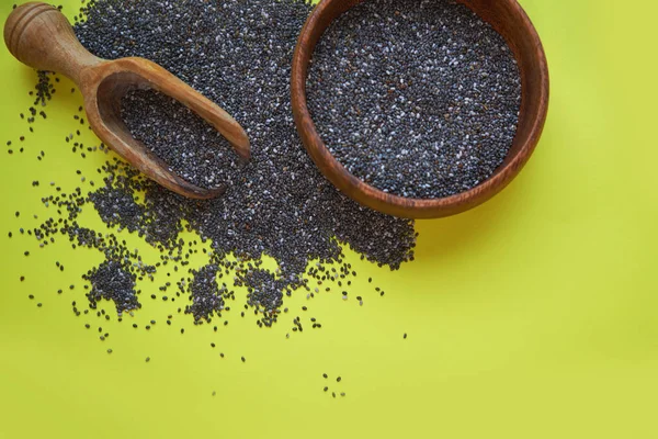 Nutritious chia seeds on a yellow background. chia seeds in bowl and a spoon on kitchen table top view. Healthy and diet superfood product.
