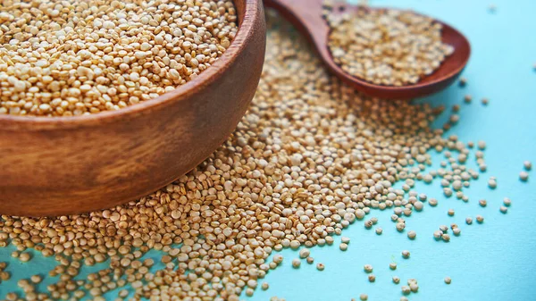 Białe nasiona quinoa na niebieskim tle. Quinoa w misce i łyżkę na stole kuchennym widoku z góry. Zdrowe i dietetyczne produkty Superfood. — Zdjęcie stockowe