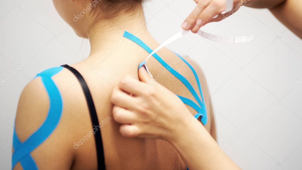 woman massage therapist applying kinesio tape to the shoulders and neck of an client in a bright medical office