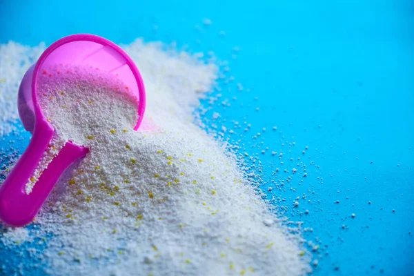 Measuring scoop with laundry powder on blue background