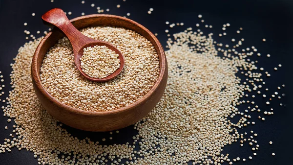 Białe nasiona quinoa na czarnym tle. Quinoa w misce i łyżkę na stole kuchennym widoku z góry. Zdrowe i dietetyczne produkty Superfood. — Zdjęcie stockowe