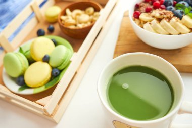 Yeşil çay, kahvaltı manzaralı beyaz arka plan. Böğürtlenli yulaf ezmesi, tahta tepside tost, fındık, kahve.