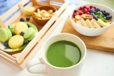 Yeşil çay, kahvaltı manzaralı beyaz arka plan. Böğürtlenli yulaf ezmesi, tahta tepside tost, fındık, kahve.